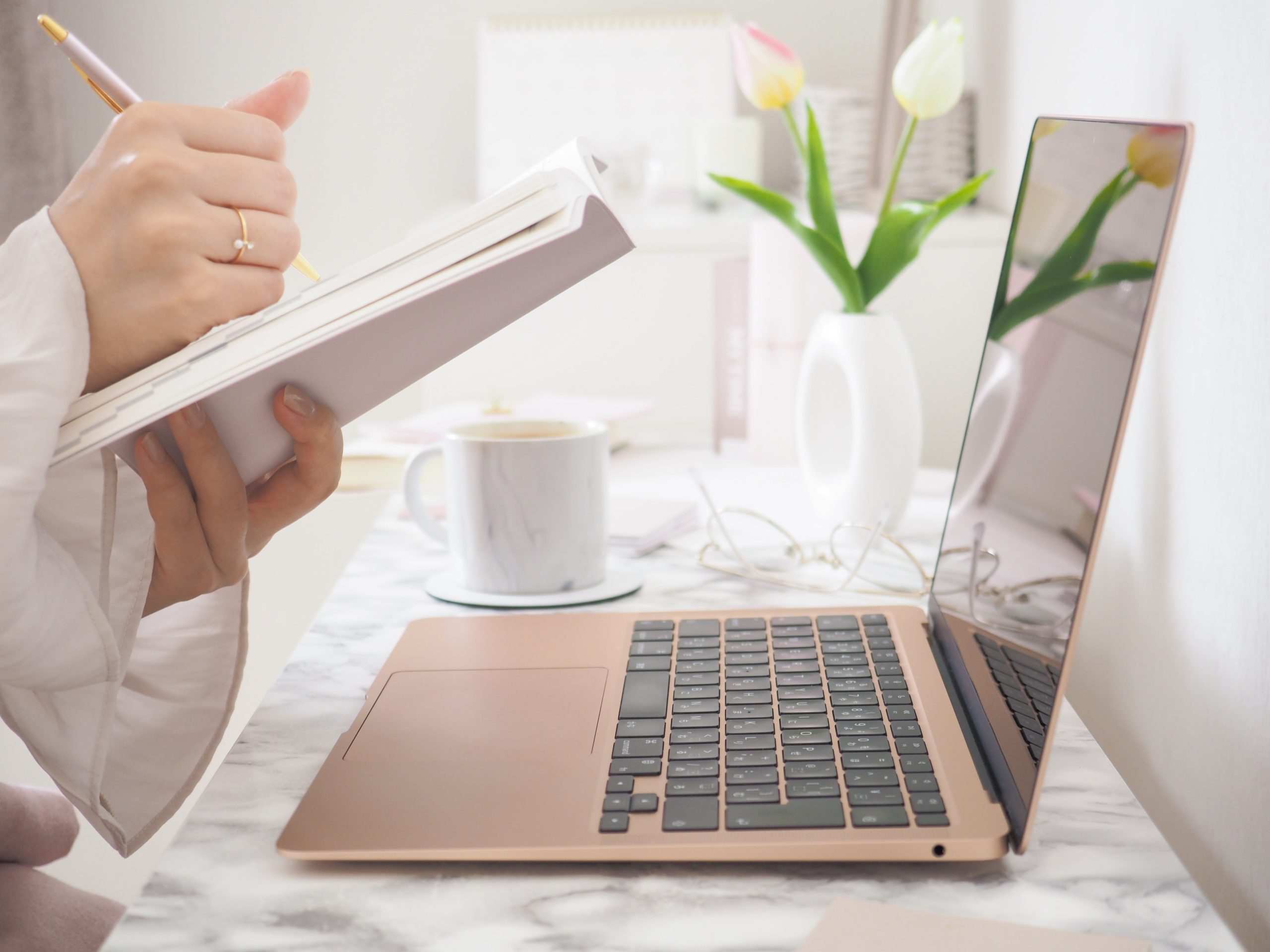 Woman sitting in front of laptop, taking notes on a notepade